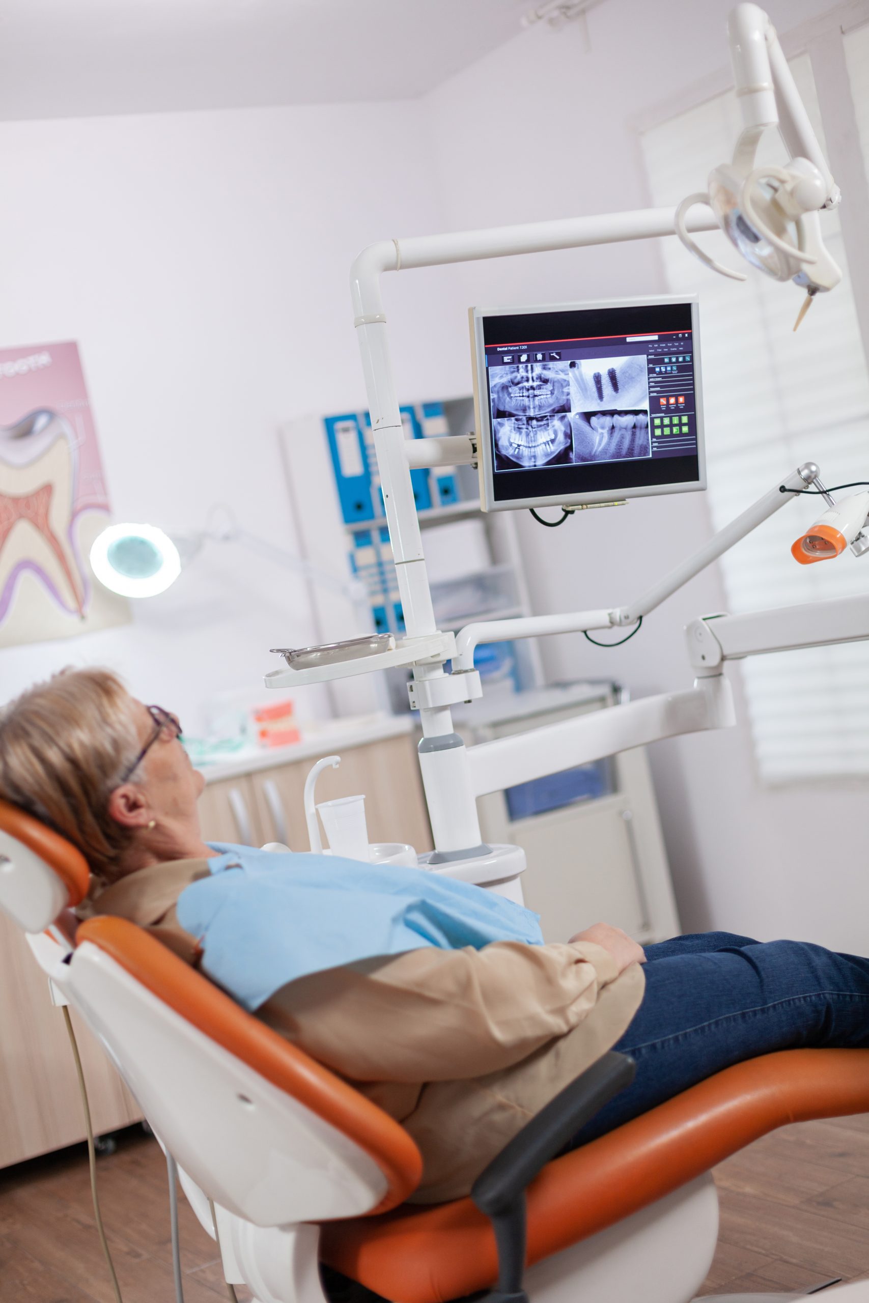 Senior woman waiting stomatolog sitting on orange chair for consultation. Elderly patient during medical examination with dentist in dental office with orange equipment.